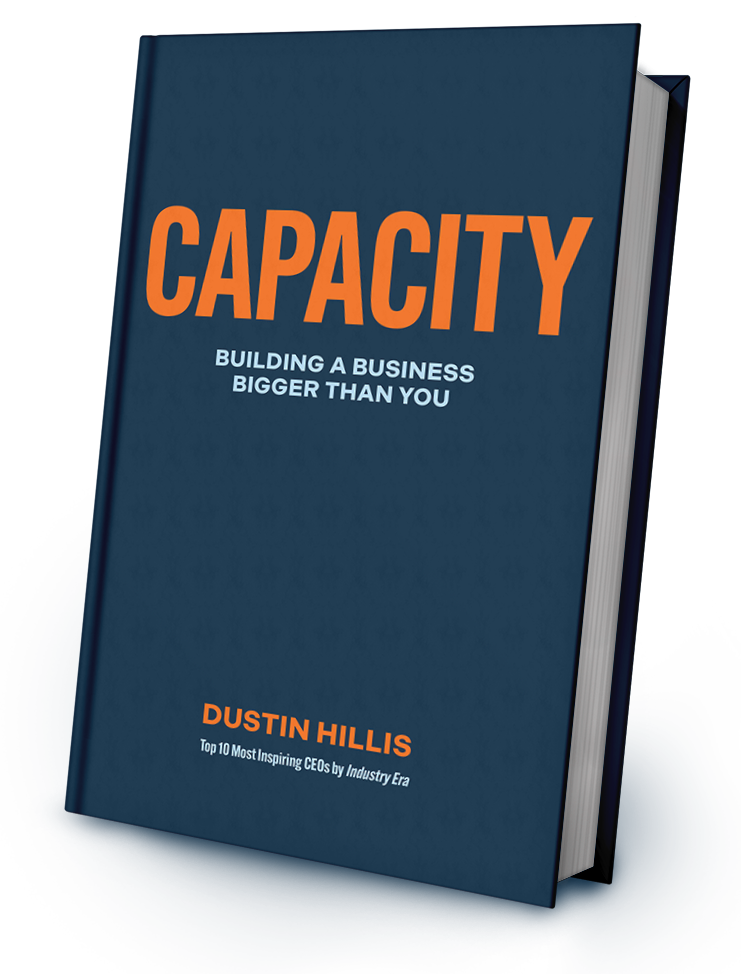 A hardcover book titled "CAPACITY: Building a Business Bigger Than You" by Dustin Hillis is shown standing upright against a white background.