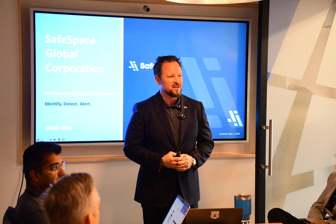 A man in business attire gives a presentation about SafeSpace Global Corporation's AI-powered safety platform to a small group in a conference room.